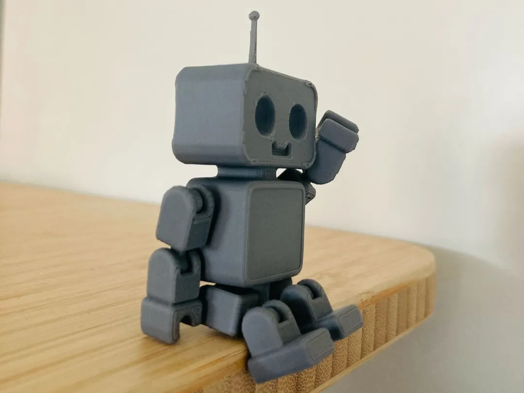 Articulated robot printed in grey, print-in-place joints, sitting on a wooden shelf edge