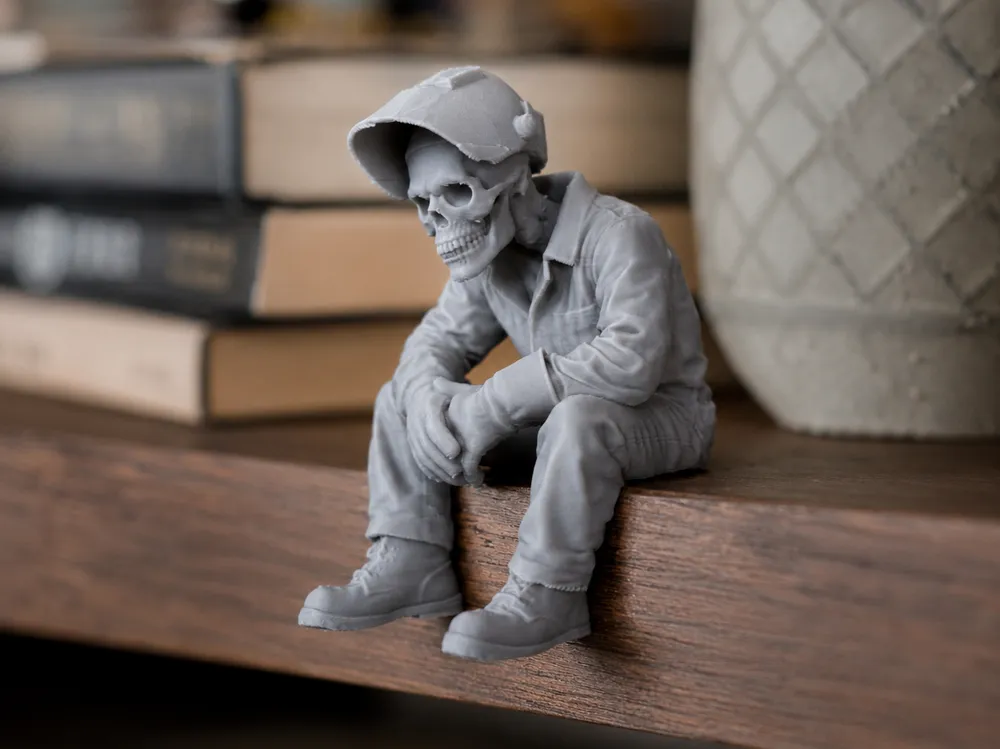 A small skeleton figure in a cap sitting on the edge of a shelf beside books