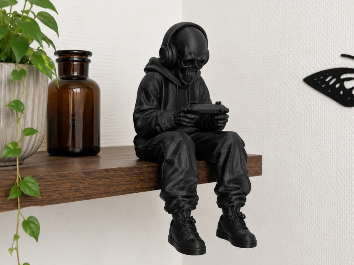 Hooded skeleton with headphones playing a handheld console, sitting on a shelf